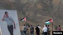 FILE - Jordanian visitors walk next to a poster depicting Jordanian King Abdullah during their visit to Baquora area in Jordanian border side, in the border area between Jordan and Israel, Nov. 13, 2019. 