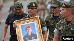 An honor guard hold up a picture of Samarn Poonan, 38, a former member of Thailand's elite navy SEAL unit who died working to save 12 boys and their soccer coach trapped inside a flooded cave as family members weep at a airport, in Rayong province, Thailand, July 6, 2018.