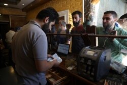 FILE - People exchange money in the city of Idlib, Syria, June 20, 2020. In the northwestern province of Idlib, the last remaining Syrian rebel stronghold, some people have started using the Turkish Lira instead of the Syrian pound.