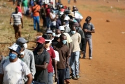 FILE - People wearing protective face masks stand in a queue to receive food aid amid the spread of the coronavirus pandemic, at the Itireleng settlement, near Pretoria, South Africa, May 20, 2020.