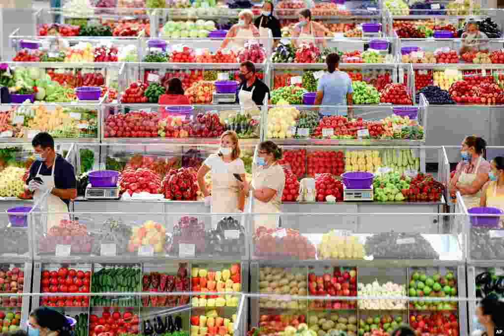 Fruit and vegetable vendors, wearing masks to help stop the spread of COVID-19, wait for customers at a market in Bucharest, Romania.