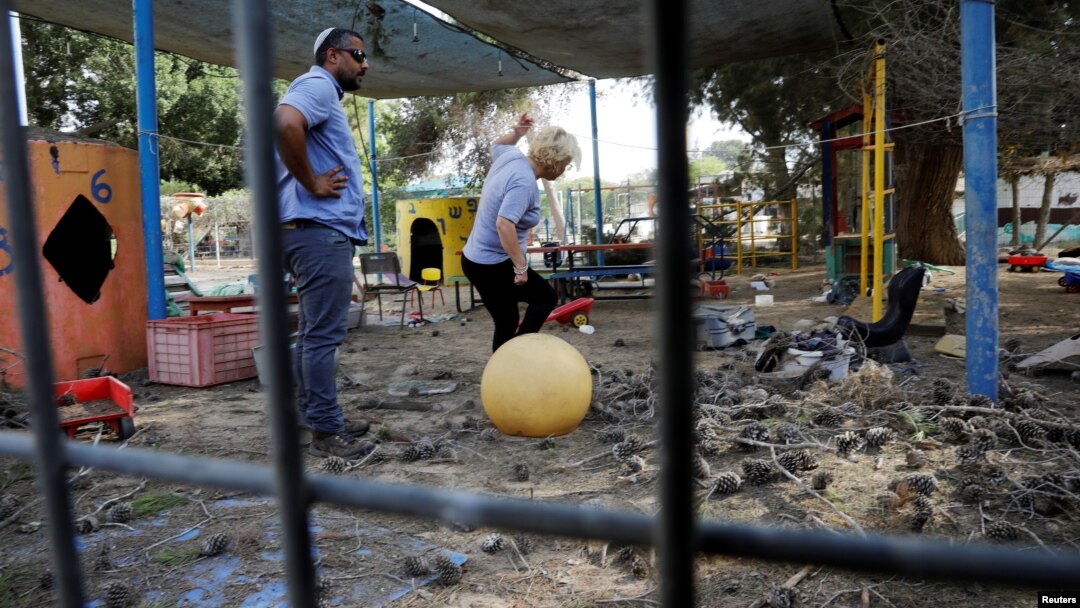Dua orang pengunjung berdiri di halaman taman kanak-kanak yang rusak akibat hantaman peluru mortir yang ditembakkan dari Jalur Gaza yang mendarat di dekatnya, di Kibbutz, di sisi Israel dari perbatasan Israel-Gaza, 29 Mei 2018.