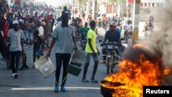 Manifestan ki te rasanble dèyè yon barikad pandan yo t ap pwoteste kont gouvènman Preidan Jovenel Moise la.