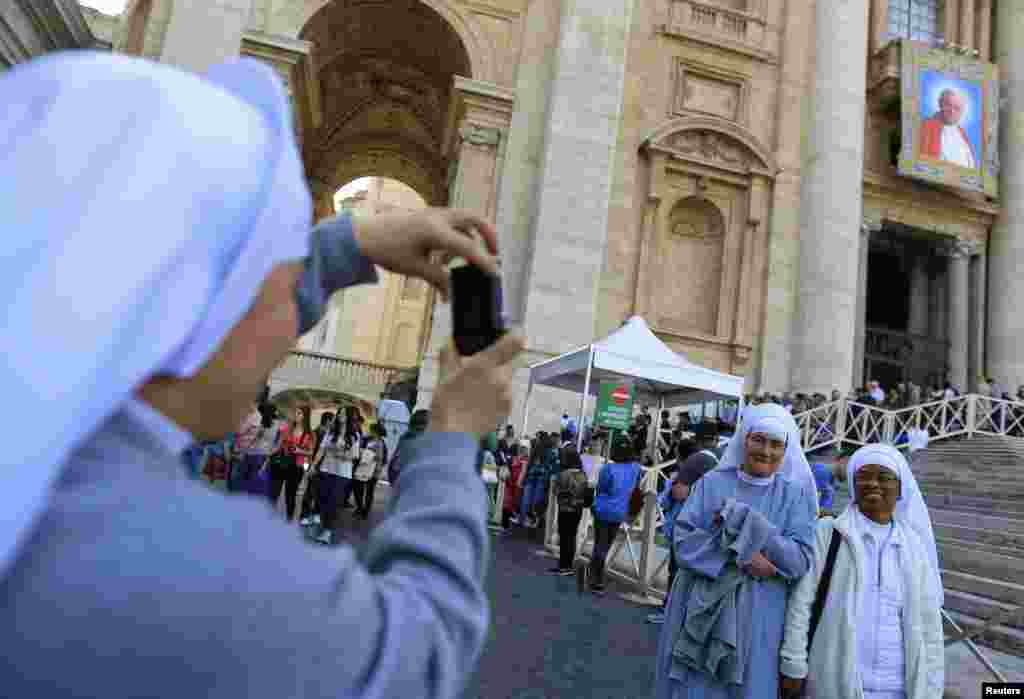 Nuns pose in front of a tapestry featuring Pope John Paul II in St. Peter&#39;s Square at the Vatican.