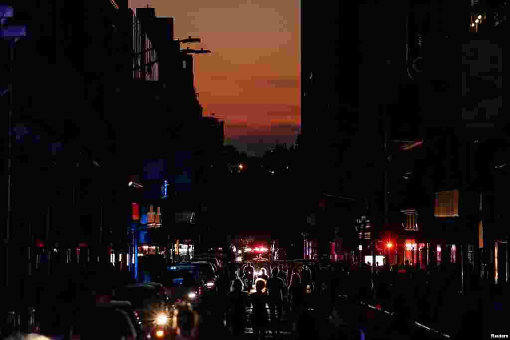 People walk along a dark street near Times Square area, as a blackout affects buildings and traffic during widespread power outages in the Manhattan borough of New York, July 13, 2019. 
