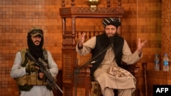 An imam speaks next to an armed Taliban fighter during Friday prayers at the Abdul Rahman Mosque in Kabul, following the Taliban's takeover of Afghanistan.