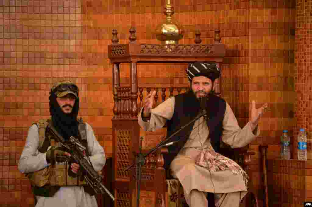 An Imam speaks next to an armed Taliban fighter during Friday prayers at the Abdul Rahman Mosque in Kabul, following the Taliban&#39;s stunning takeover of Afghanistan.