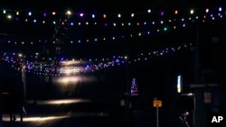 A convenience store worker sweeps the doorstep and sidewalk under the glow of Christmas lights on Main Street in Farmington, N.H., March 19, 2020.