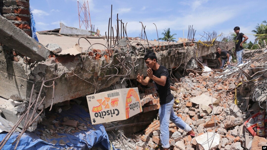 Seorang pria mengambil sebuah kotak makanan dari bawah reruntuhan bangunan pasca gempa yang menghantam wilayah Pidie Jaya, provinsi Aceh, Indonesia, 7 Desember 2016 (AP Photo/Heri Juanda).