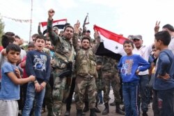 FILE - In this photo released by the Syrian official news agency SANA, Syrian troops celebrate and hold the Syrian national flag as they deploy in the city of Kobani, Syria, Oct. 17, 2019.