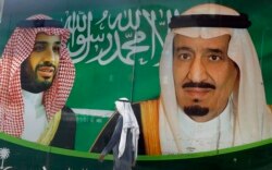 FILE - A man walks past a banner showing Saudi King Salman, right, and his Crown Prince Mohammed bin Salman, outside a mall in Jiddah, Saudi Arabia, March 7, 2020.