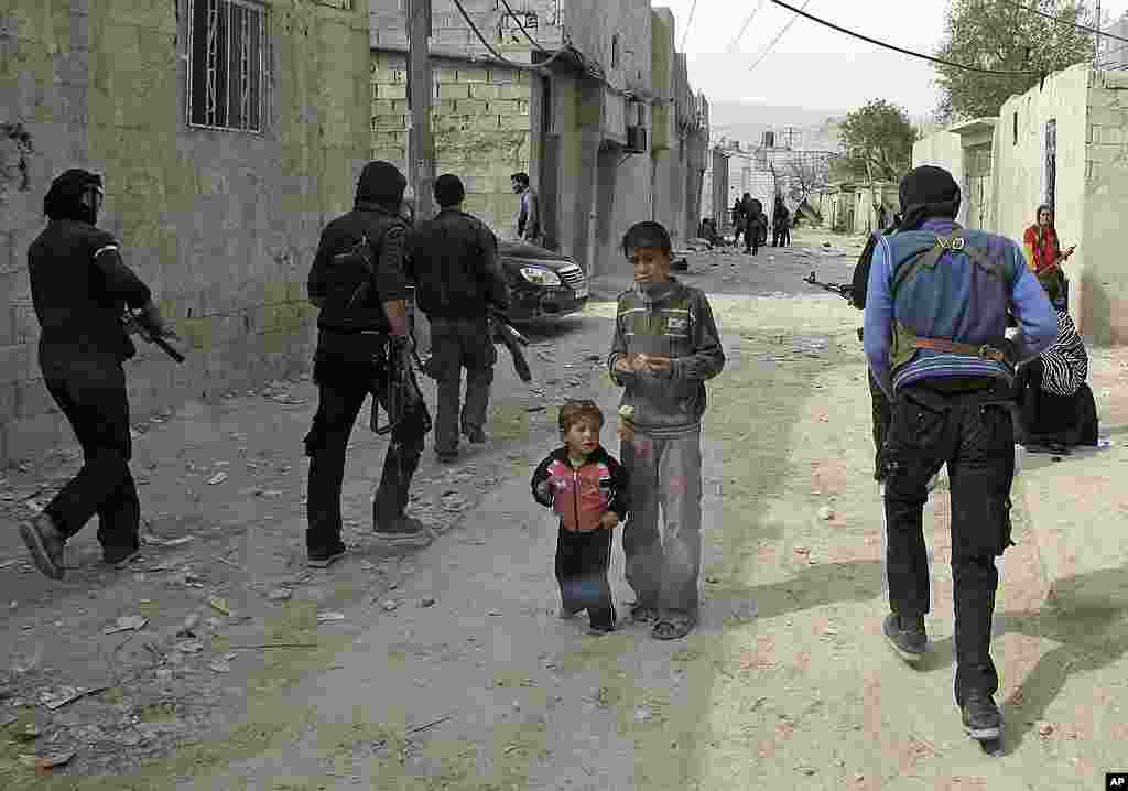 Syrian boys watch Free Syrian Army fighters move through a neighborhood in Damascus. (AP)