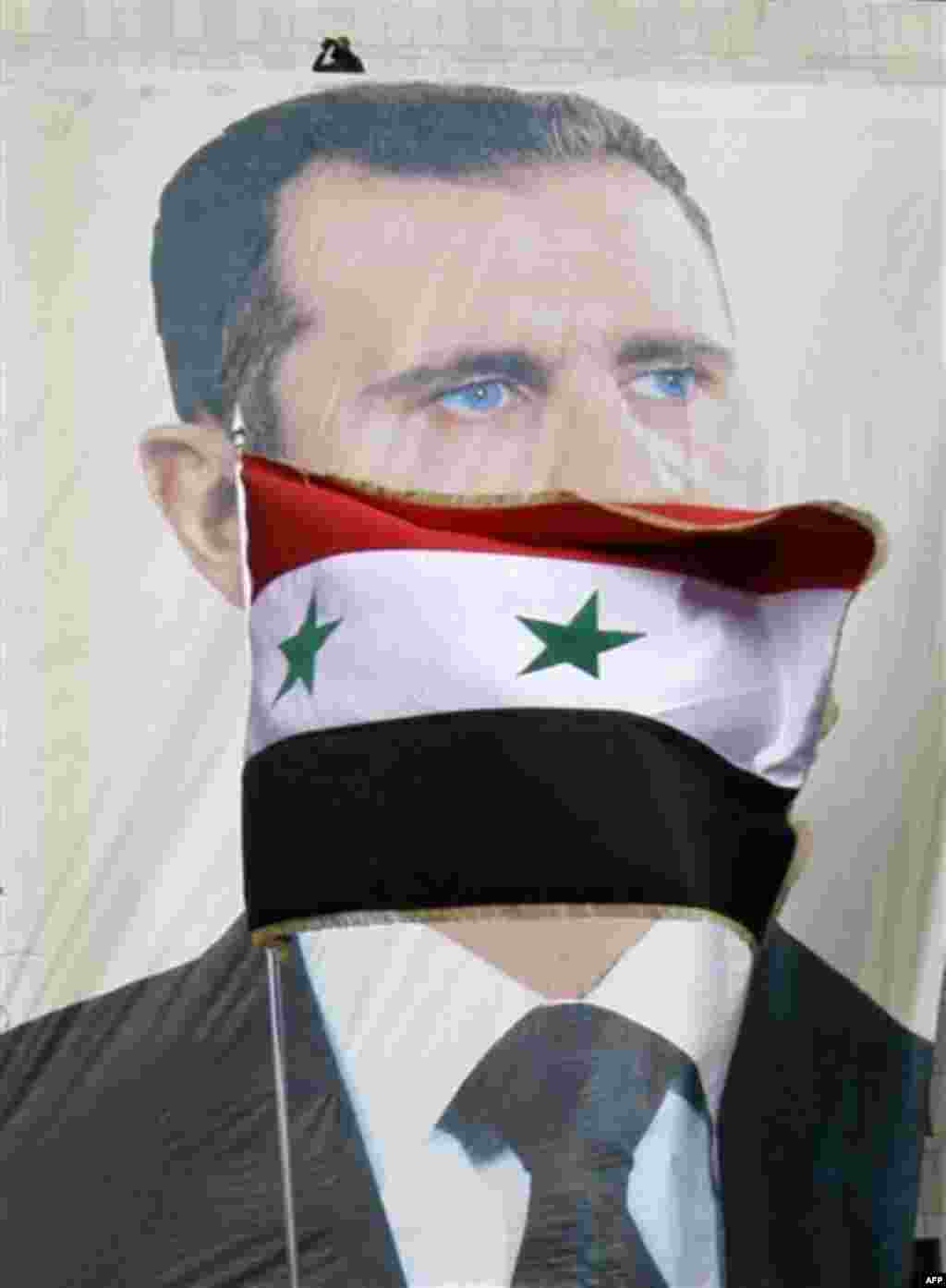 A Syrian flag flies as pro-Syrian regime protesters hold a rally in support of President Bashar Assad, pictured in the large banner, in Damascus, Syria, Friday, Dec. 9, 2011. Syrian forces killed at least six people _ including two children _ as they fire