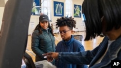 Zari Gedeon, de 11 años, centro, escucha a un trabajador electoral mientras ayuda a su madre, Lauren Gedeon, de Washington, a la izquierda, a enviar su voto junto, en la escuela secundaria Ida B. Wells, en Washington. (Foto AP/Jacquelyn Martín)