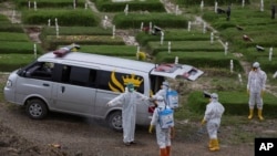 Seorang pekerja menyemprot rekannya dengan disinfektan setelah menguburkan seseorang yang diduga meninggal karena virus Covid-19 di pemakaman di Medan, Sumatera Utara, Selasa, 24 November 2020. (Foto AP / Binsar Bakkara)
