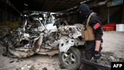 FILE - A Turkey-backed Syrian fighetr inspects the remains of a car that reportedly exploded in a market in the northern Syrian city of Afrin, killing and wounding several people, Dec. 16, 2018.