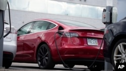 A car made by the automaker Tesla, a 2021 Model 3 sedan, is connected to a charger where Tesla vehicles are sold on June 27, 2021, in Littleton, Colo. (AP Photo/David Zalubowski, File)