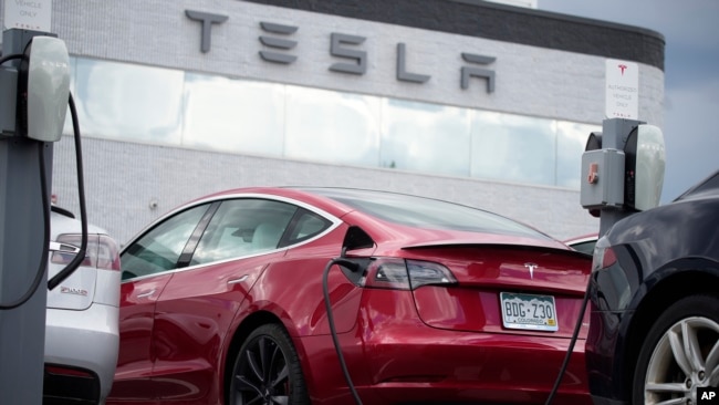 A car made by the automaker Tesla, a 2021 Model 3 sedan, is connected to a charger where Tesla vehicles are sold on June 27, 2021, in Littleton, Colo. (AP Photo/David Zalubowski, File)