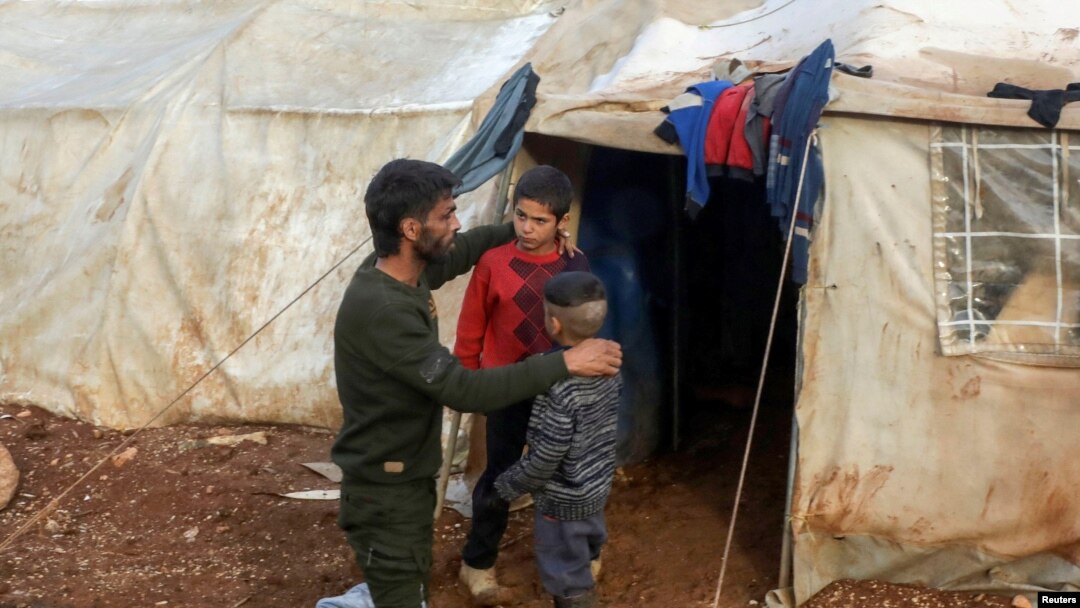 FILE - A father talks with his children outside of a tent at an internally displaced Syrian camp, in northern Aleppo, near the Syrian-Turkish border, Syria, Feb. 17, 2021.