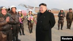 ຜູ້ນຳເກົາຫລີເໜືອ ທ່ານ Kim Jong Un ຢືນຍິ້ມໃນ ຂະນະທີ່ ຢ້ຽມຢາມ ນັກບິນຜູ້ຍິງ.