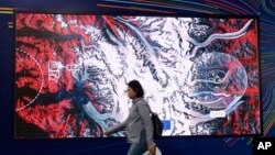 In this Dec. 11, 2018 photo a participant in U.N. climate conference walks by a photo of a satellite in Katowice, Poland.