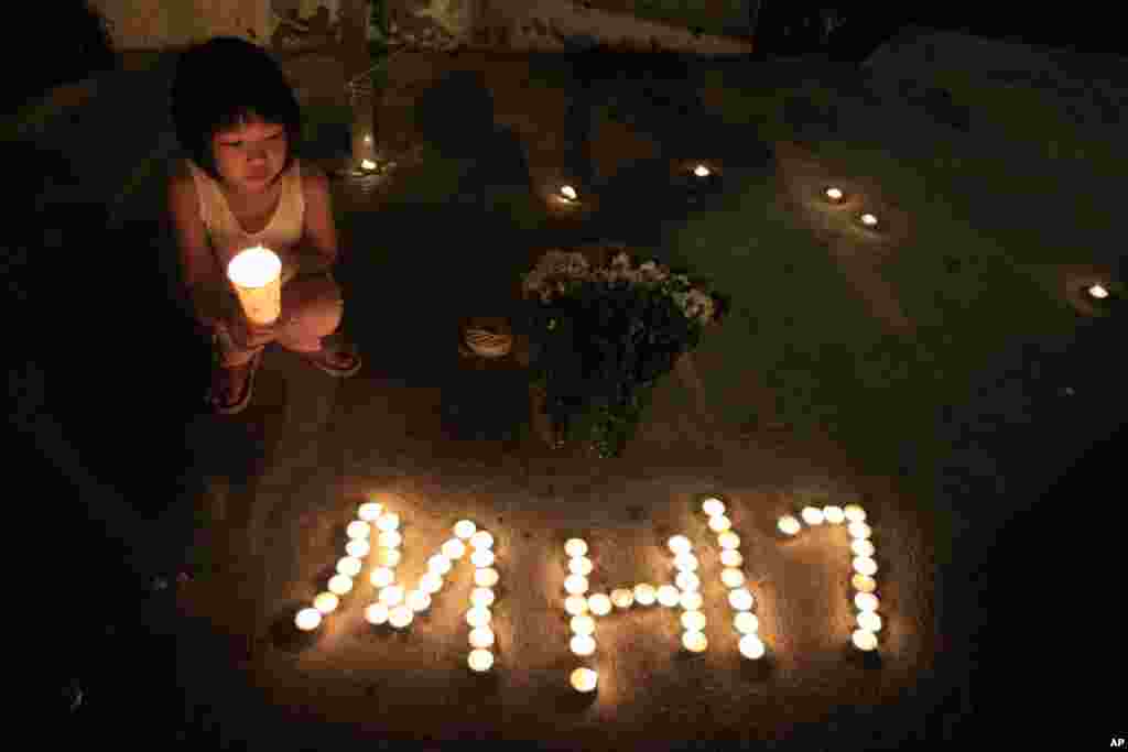 A girl holding a candle squats next to candles forming MH17 during an event to mourn the victims of the crashed Malaysia Airlines Flight 17, in Kuala Lumpur, Malaysia, July 20, 2014. 