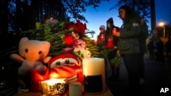 Student light candles next to flowers and portraits of victims, outside the Perm State University following a campus shooting in Perm, about 1,100 kilometers (700 miles) east of Moscow, Russia, Sept. 21, 2021. 