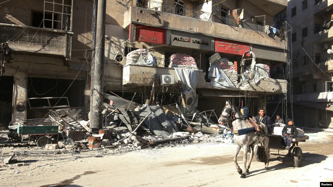 Warga mengendarai kereta kuda di dekat bangunan rumah sakit al-Hakeem di Aleppo, Suriah yang hancur akibat serangan udara (19/11). 