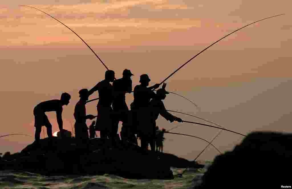 Men fish on top of a rock in the sea in Colombo, Sri Lanka.