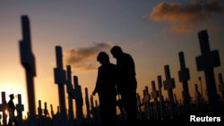 FILE - A couple grieves at a grave in a cemetery Coral Gables, Florida, Feb. 16, 2008. A new study shows that suicide rates in the U.S. jumped 24 percent between 1999 and 2014.