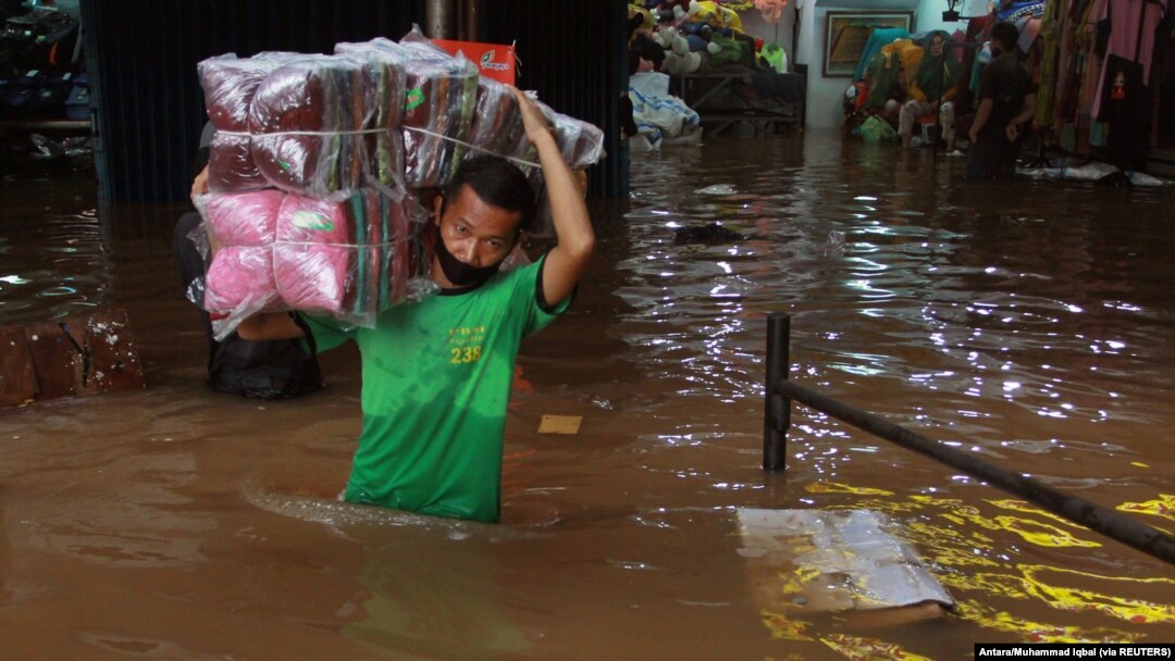 Seorang pedagang mengangkut barang-barangnya melalui air di pasar di daerah yang terkena banjir menyusul hujan lebat di Jakarta, 20 Februari 2021. (Foto: Antara/Muhammad Iqbal via REUTERS