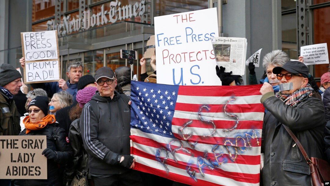 FILE - Demonstrators stand with U.S. flags and signs in a show of solidarity with the press in front of The New York Times building in New York, Feb. 26, 2017.