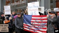 FILE - Demonstrators stand with U.S. flags and signs in a show of solidarity with the press in front of The New York Times building in New York, Feb. 26, 2017.