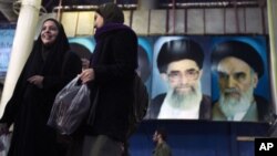 Iranian women walk in front of the pictures of Ayatollah Ruhollah Khomeini, the founder of the Islamic Republic (R) and Iran's Supreme Leader Ayatollah Ali Khamenei during the anniversary ceremony of Iran's Islamic Revolution at the Behesht Zahra cemetery