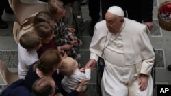 ARCHIVO - El Papa Francisco toma la mano de un niño pequeño mientras saluda a los fieles al final de su audiencia general semanal en el Aula Pablo VI, en el Vaticano, el 12 de febrero de 2025.