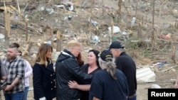 U.S. President Donald Trump is hugged by a resident who survived a tornado, as first lady Melania Trump stands by, in Beauregard, Alabama, March 8, 2019. 