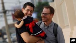 American Gordon Lake, left, and Manuel Santos, right, walk with their baby Carmen, center, at the Central Juvenile and Family Court in Bangkok, Thailand, Wednesday, March 23, 2016.