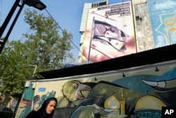 Seorang perempuan berjalan melewati spanduk anti-Israel di sebuah gedung di Lapangan Felestin (Palestina) di pusat kota Teheran, Iran, Minggu, 14 April 2024. (Foto: AP)