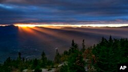 FILE - Sun rays spill through a gap between the clouds and the White Mountains as the skies begin to clear above Bartlett, N.H., Sept. 22, 2017. The first weekend of autumn in the area was unusually warm — and across the nation, the year's first freeze has been arriving further and further into the calendar. 