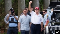 El presidente Donald Trump hace un gesto a sus partidarios reunidos para un mitin del Día de los Presidentes al salir del Trump International Golf Club, el lunes 17 de febrero de 2025, en West Palm Beach, Florida. (AP foto/Ben Curtis).