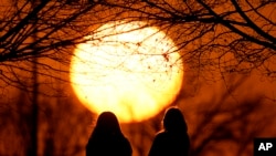 ARCHIVO - Personas miran la puesta de sol en un parque en un día inusualmente cálido, el 25 de febrero de 2024, en Kansas City, EEUU. 