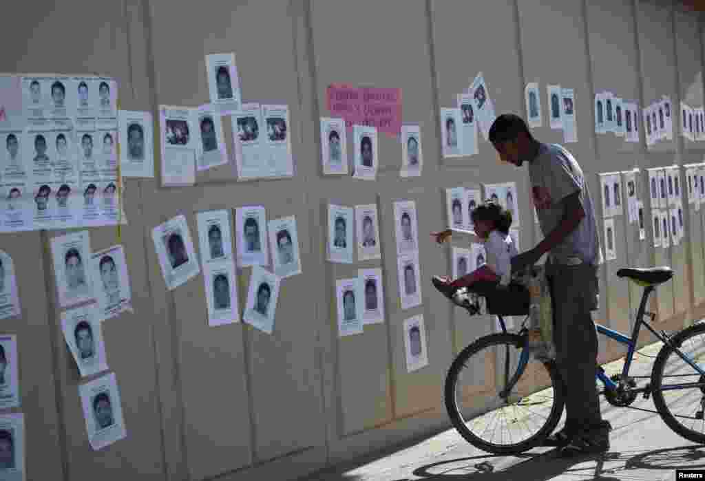 A girl points at photographs of missing students from the Ayotzinapa teachers' training college, on a wall surrounding the General Attorney's Office in Ciudad Juarez, Oct. 23, 2014.