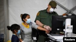 Un oficial de migración toma datos biométricos de una migrante y su hija ingresan en el área de admisión del centro de detención del Departamento de Seguridad Nacional, en el Valle del Río Grande. 30 de marzo de 2021.