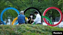 People chat next to Olympic Rings monument outside the Japan Olympic Committee (JOC) headquarters near the National Stadium, the main stadium for the 2020 Tokyo Olympic Games that have been postponed to 2021, in Tokyo, June 23, 2021.