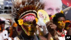 A man with a traditional headdress uses a fan to shield the sun as Pope Francis holds a holly mass at Sir John Guise Stadium in Port Moresby, Papua New Guinea, Sept. 8, 2024. 