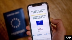 A picture taken on June 29, 2021 in Paris shows a passport behind a mobile phone whose screen bears a EU Digital COVID certificate.