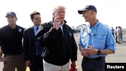 El presidente Donald Trump habla con el gobernador de Florida Rick Scott, mientras atrás al fondo esperan el administrador de FEMA, Brock Long (izq.), y el legislador republicano por Florida, Ron DeSantis. El presidente viajó al estado para visitar la zona afectada por el huracán Michael. Oct. 15. de 2018. 