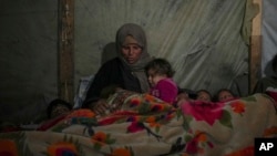 Reda Abu Zarada wraps herself and her grandchildren in blankets as they prepare to sleep in their tent at a camp in Khan Younis, Gaza Strip, Dec. 19, 2024. 