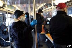 A subway rider wears a glove while holding a pole as several riders wear face masks during the coronavirus outbreak on the D train in the Brooklyn borough of New York on March 25, 2020.