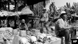 A Cambodian villager sits near human skulls recovered from debris in provincial Cambodia after government troops retook a village on Route 3, southwest of Phnom Penh in 1973. The skeletal remains were those of civilians and soldiers killed by Khmer commun